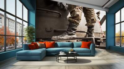 Legs of a soldier standing on metal tank, on a battlefield. Wearing military boots and woodland camo pants (camouflage trousers). Wall mural