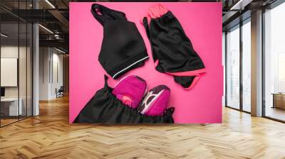 Womens gym wear. Sports bra, shorts for workout and training shoes in a black bag. Ladies fitness clothes, apparel equipment set. Healthy lifestyle exercise composition on pink background. Wall mural