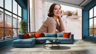 Adorable dark-eyed girl laughing at balcony. Photo of cheerful caucasian woman with beautiful smile. Wall mural