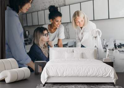 African and european girls looking at computer screen while blonde lady reading documents. Indoor portrait of asian student in glasses talking with female friends in uniersity. Wall mural