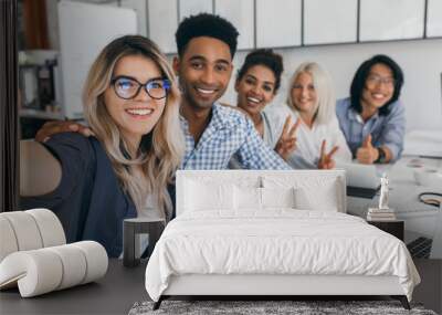 African and european girls posing with peace sign while blonde lady making selfie in conference hall. Young african web-developer having fun with colleagues and smiling for photo. Wall mural