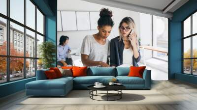 African girl in white t-shirt found mistake in the report. Worried female office worker calling colleague to solve working problems while her co-workers doing their job. Wall mural