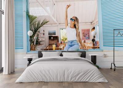 barefooted girl in vintage jeans sitting on window sill. photo of emotional blonde woman in casual a Wall mural