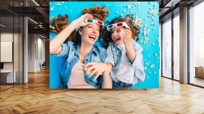 Brightful stylish image from above excited mother and daughter laying on blue floor in popcorn, laughing  in 3D glasses. Happy family time, entertainment pretty mum with kid, expressing happiness Wall mural