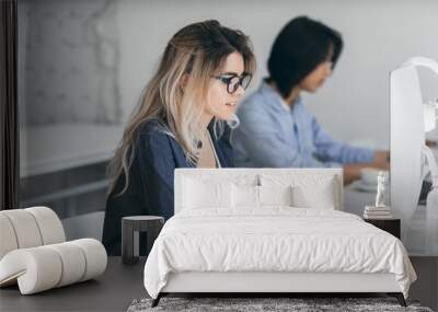 Busy female freelancer with long hair working with tablet and drinking coffee. Indoor portrait of concentrated japanese student using computer in classroom. Wall mural