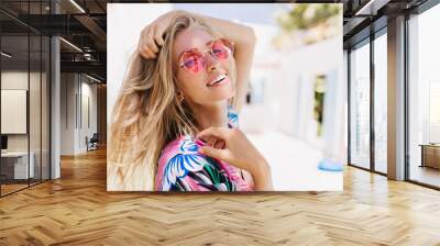 Close-up portrait of magnificent caucasian girl in round pink sunglasses. Lovable long-haired blonde woman enjoying life and having fun at resort. Wall mural