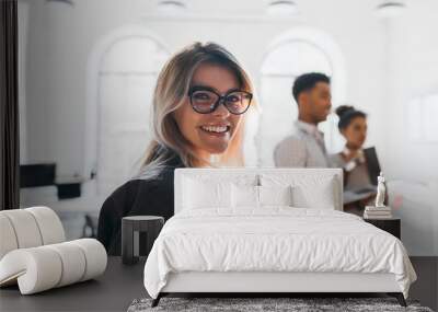 Close-up portrait of smiling female student in trendy glasses holding documents on blur background. Black young man working as manager carrying laptop to office. Wall mural