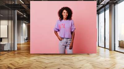 Confident appealing girl standing with hand in pocket. Studio portrait of shy african lady in purple shirt. Wall mural