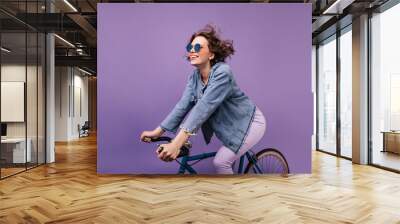 Dark-haired joyful lady chilling during photoshoot on bike. Winsome caucasian girl with wavy hair sitting on bicycle. Wall mural