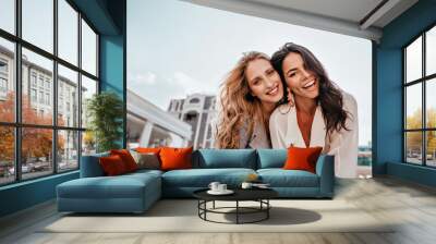 Ecstatic long-haired girls posing in spring day on sky background. Outdoor photo of two good-looking female friends. Wall mural