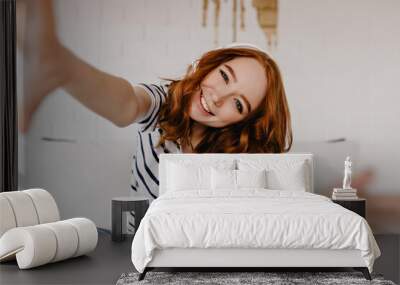 ecstatic red-haired girl making selfie and laughing. emotional caucasian lady in casual attire expre Wall mural