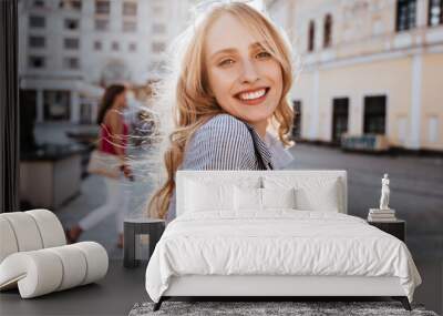 Emotional blonde woman posing with happy smile on the street. Debonair caucasian girl enjoying photoshoot on city background. Wall mural