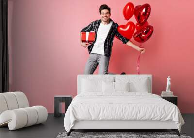 Emotional young man jumping on pink background. Brunette guy with red balloons expressing happiness. Wall mural