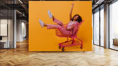 Enthusiastic brunette girl expressing sincere positive emotions. Studio shot of beautiful woman sitting in shopping cart. Wall mural