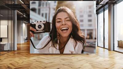 Enthusiastic female photographer looking to camera with pleased smile. Excited brunette girl with camera making photos. Wall mural