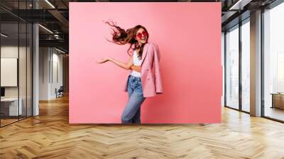 Excited good-looking girl in sunglasses dancing in studio. Ginger blissful woman posing on rosy background with hair waving. Wall mural