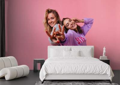 Fascinating emotional girls laughing to camera and having fun. Studio portrait of joyful friends isolated on bright background. Wall mural