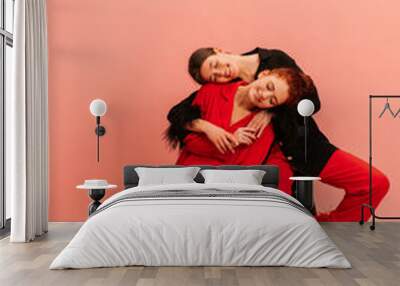 Full-length two young caucasian girls eyes closed are sitting in studio with heads on top of each other. Brunette and the redhead are wearing black and red suits. People's emotions, lifestyle concept. Wall mural