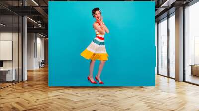 Full length view of pinup girl in striped dress. Studio shot of brunette lady dancing on blue background. Wall mural