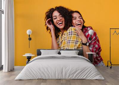 Girls in stylish street clothes sincerely laugh at each other's jokes. Girlfriends happily pose for common photo in studio Wall mural