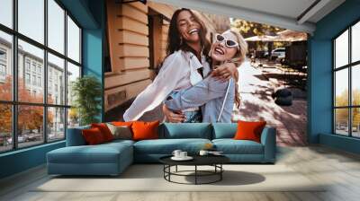 Glamorous woman in sunglasses embracing her sister. Outdoor photo of wonderful girls spending weekend together. Wall mural