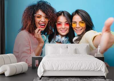 Gorgeous young woman in sunglasses posing with pleasure near brunette female friends. Cheerful asian girl in yellow outfit chilling with ladies during joint photoshoot. Wall mural