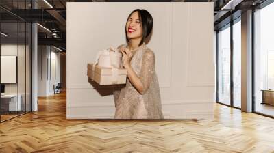 happy young asian girl holding gift boxes smiling with her eyes closed over white background. brunet Wall mural