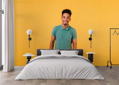 Indoor portrait of smiling black man standing with hands in pockets. Studio shot of blithesome african guy isolated on yellow background. Wall mural