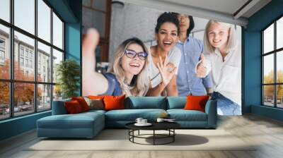 Indoor portrait of young developers fooling around in office during break. Amazing female worker of international company making selfie with african and asian colleagues. Wall mural