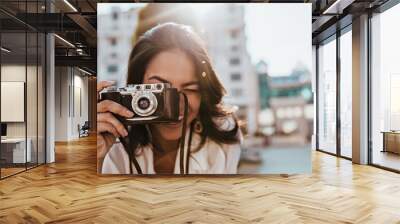 Inspired female photographer with dark hair working outdoor. Portrait of smiling girl with camera making photos on the street. Wall mural