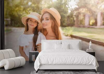 inspired young woman with beautiful tan posing with pleasure near little daughter in stylish attire. Wall mural