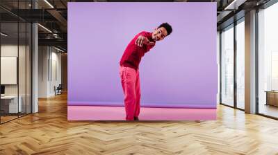 Interested black boy in spring attire pointing finger to camera. Studio portrait of brunette african guy standing on purple background. Wall mural