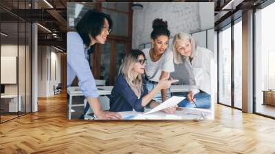 Joyful office workers of international company preparing for presentation together. Asian male manager looking at computer screen while his blonde european colleague explains something. Wall mural