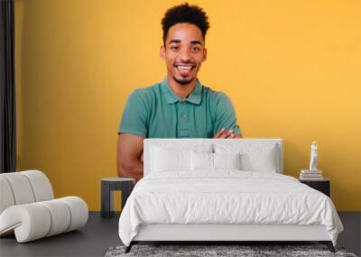 Laughing african guy with trendy haircut posing on bright yellow background with arms crossed. Studio shot of black man smiling to camera during photoshoot. Wall mural