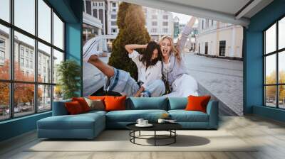 Laughing brunette woman having fun with her best friend in spring morning. Carefree sisters in good mood smiling on city background. Wall mural