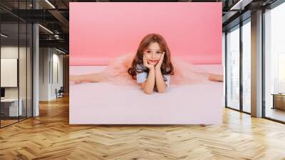 Leisure time of joyful charming little girl making gymnastics split on floor on pink background. Elastic cute child in tulle skirt  with long brunette hair smiling to camera, expressing cheerful mood Wall mural