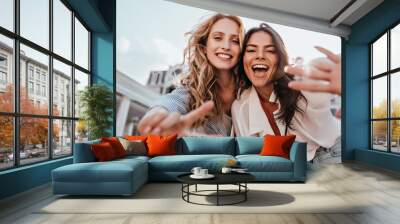 Lovable caucasian girls expressing positive emotions to camera. Outdoor photo of refined sisters posing on sky background. Wall mural