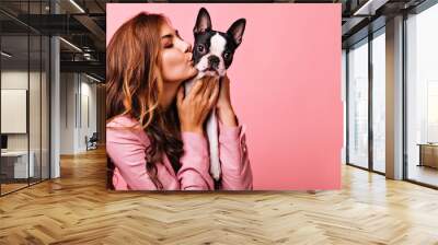 Lovely female model kissing funny bulldog puppy. Indoor portrait of refined dark-haired girl posing on pink background with dog. Wall mural