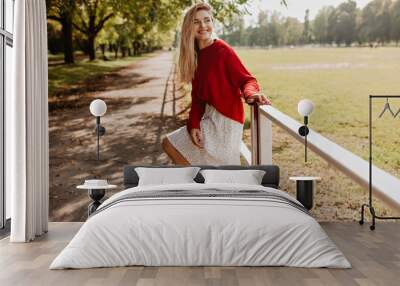 Lovely girl in red nice shoes and white dress enjoying herself in the park. Beautiful blonde woman posing playfully near yellow fallen leaves. Wall mural