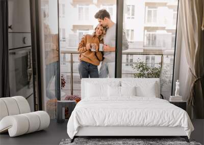 Man embracing wife at balcony. Relaxed couple drinking coffee in weekend. Wall mural