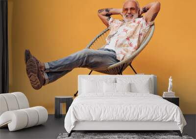 Man has rest and poses with his suitcase. Gray-haired handsome guy sits on chair and relaxes with smile on his face Wall mural