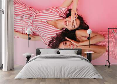 On pink isolated background beautiful dark-skinned girls with cute smiles are having fun and posing in front of camera lying on their backs Wall mural