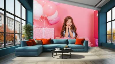 Portrait cute birthday kid expressing to camera suround big giftboxes, balloons isolated on pink background. Amazing little girl with long brunette hair smiling with present on knees Wall mural