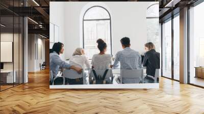 Portrait from back of african girl in white shirt with backpack resting with friends after lessons. Indoor photo of young people discussing something in conference hall with big windows. Wall mural