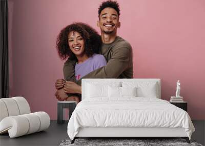 Portrait of happy couple hugging and smiling on pink background. Dark-skinned woman in purple sweater and her boyfriend posing on isolated Wall mural