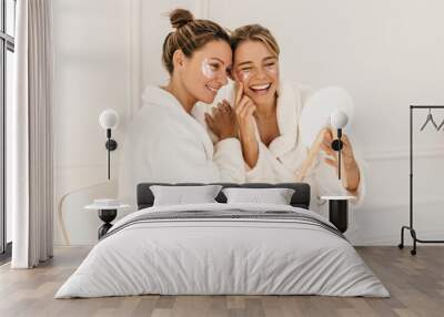 Pretty caucasian young women wear bathrobes admire themselves looking in mirror on white background. Blondes use eye patches for dark circles. Beauty and personal care, skin and face care concept Wall mural