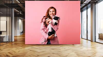 Pretty white girl holding bulldog and laughing to camera. Blithesome caucasian woman with dog having fun in studio. Wall mural