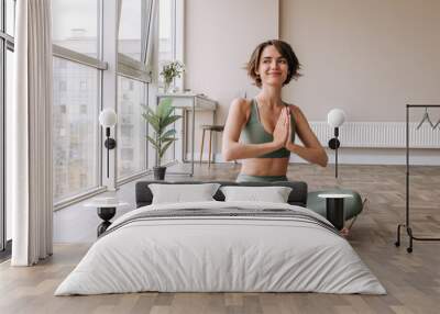 Pretty young brunette woman practicing yoga at home . Caucasian cute girl looking away and smiling wearing green sportswear sitting on the floor. Concept of leisure, relaxation, workout  Wall mural