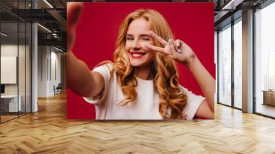 Romantic young woman with trendy manicure posing on red background. Adorable fair-haired lady laughing to camera. Wall mural