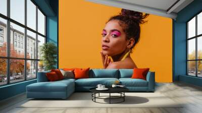 Sensual african girl with pink makeup looking over shoulder. Studio shot of curious black model isolated on orange background. Wall mural